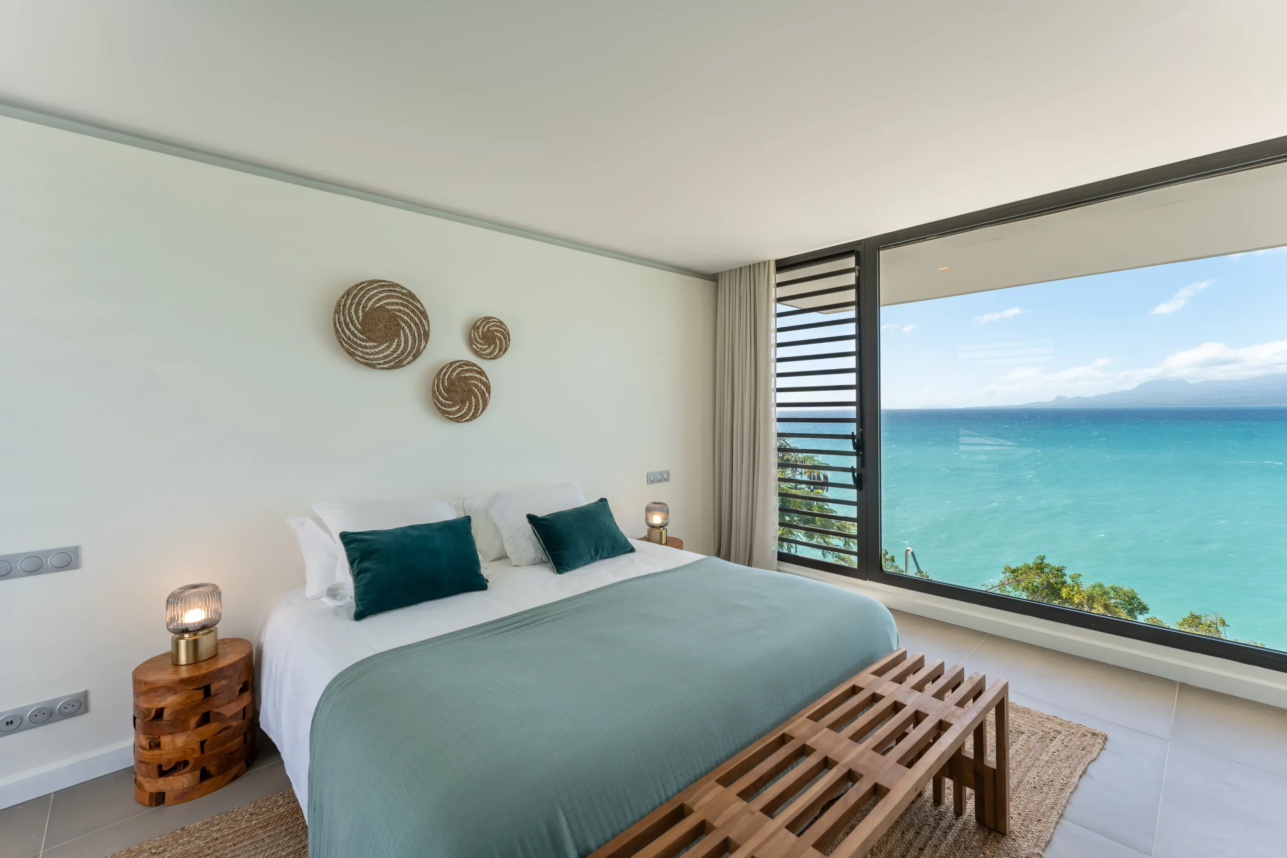 chambre de la villa guacana avec grande baie vitrée donnant vue sur la mer turquoise de Guadeloupe et le relief de la basse terre